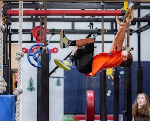 A baby in a striped tank top is hanging from gymnastic rings