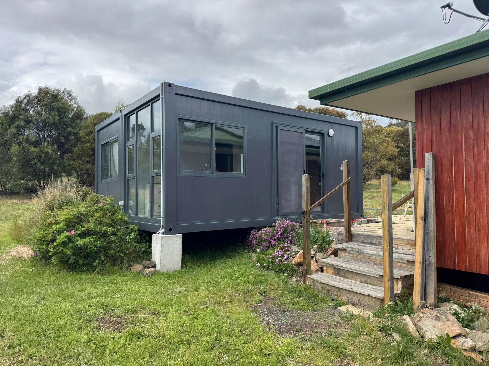 A modern modular structure made from shipping containers with wood cladding, a central deck, and a flat roof outdoors.
