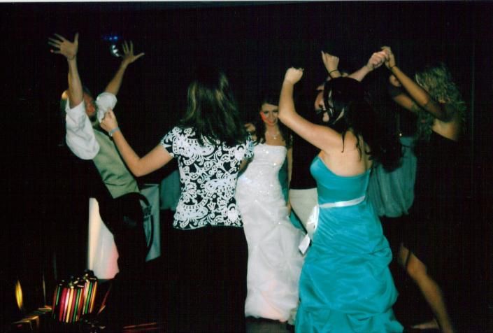 People dancing with raised arms at a party, with a woman in a turquoise dress in the foreground