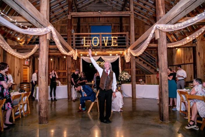 Rustic wedding reception with a couple under a glowing “LOVE” sign in a barn-style venue