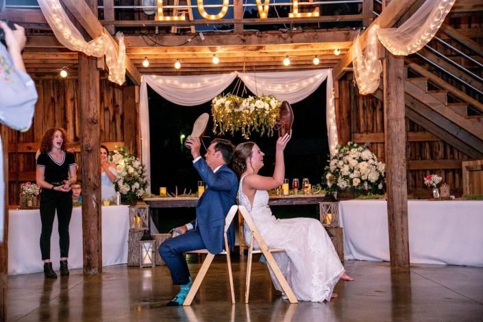 Bride and groom seated back-to-back in a rustic wedding venue with floral décor and draped lights