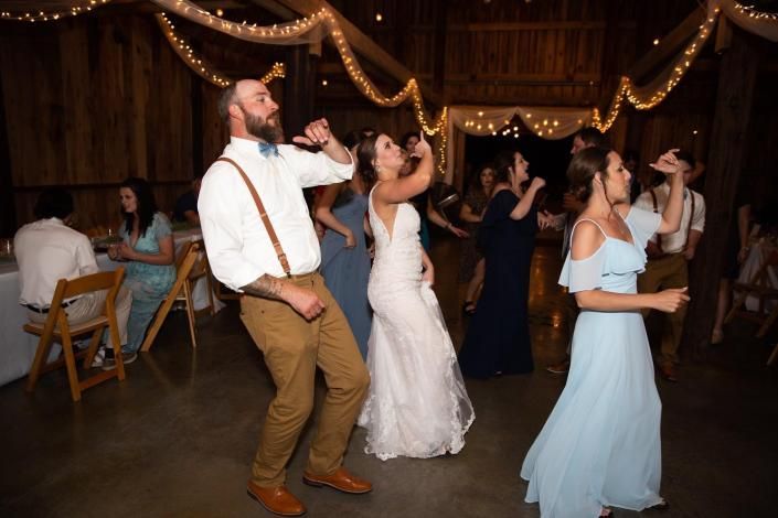 Wedding guests dancing in a warmly lit reception hall with string lights and wooden walls