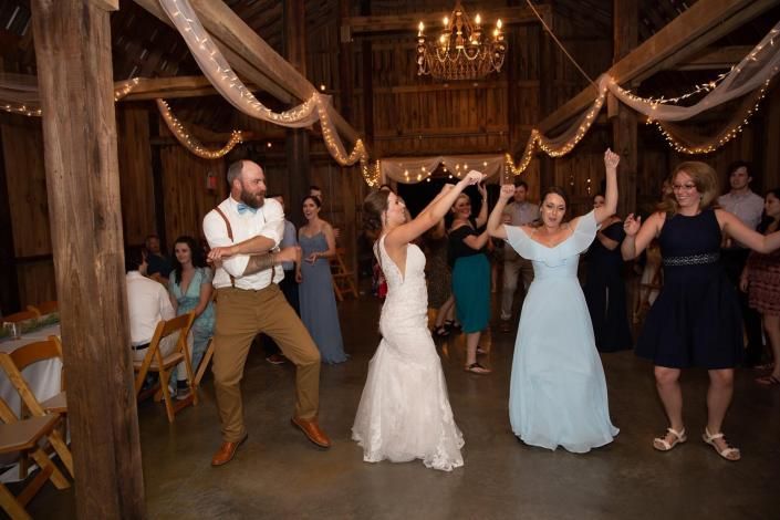 Wedding guests dancing in a rustic barn reception, with the bride and bridesmaids in the center