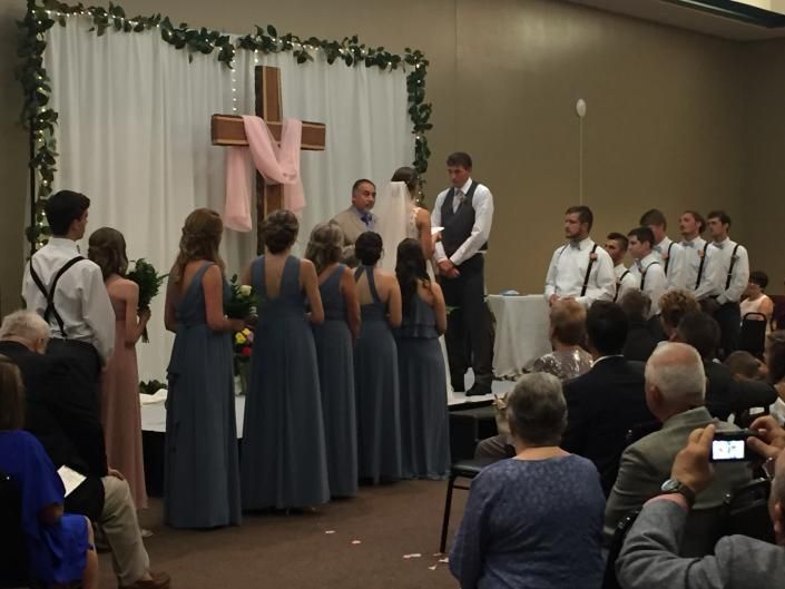Wedding ceremony with bride and groom beneath a pink cross, guests standing around them