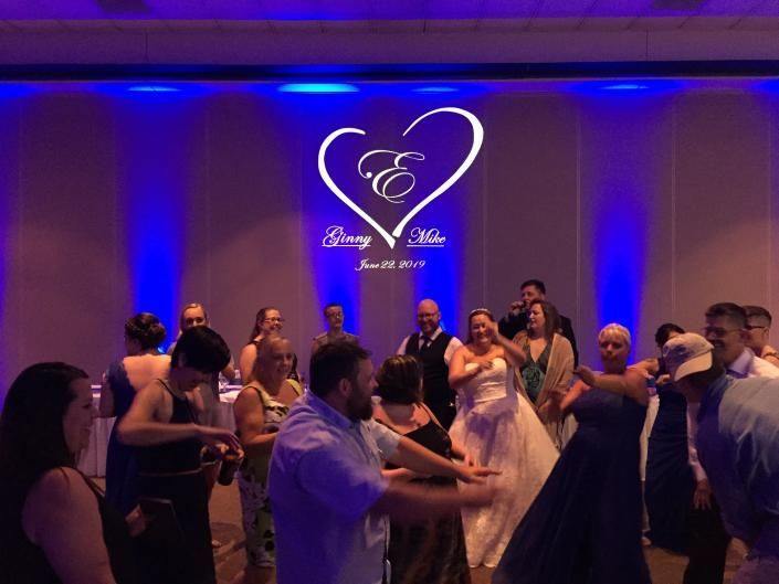 Wedding reception dance floor with guests dancing under blue lights and a heart-shaped monogram on the wall