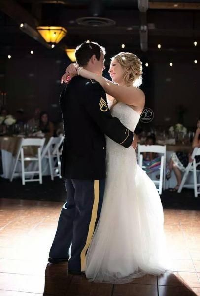 Couple slow dancing at a dimly lit wedding reception, bride in white dress and groom in dark suit.