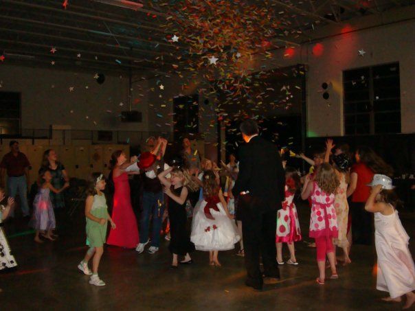 Children dancing at a party while confetti rains down in a dimly lit room