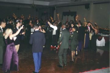 Crowded dance floor at a formal event, people in dark attire dancing and clapping in a dimly lit hall
