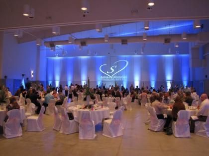 Banquet hall with round tables, seated guests, and a blue-lit stage backdrop with a projected logo
