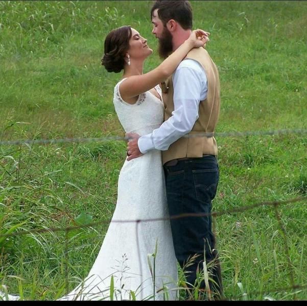 Bride and groom embracing in a grassy field, facing each other in wedding attire