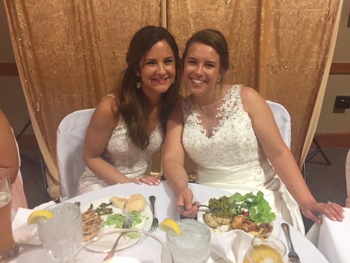 Two women in white dresses smiling at a banquet table with plates and drinks.