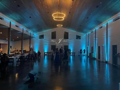 Large modern event hall with blue uplighting, chandeliers, and a few people gathered near the back wall.