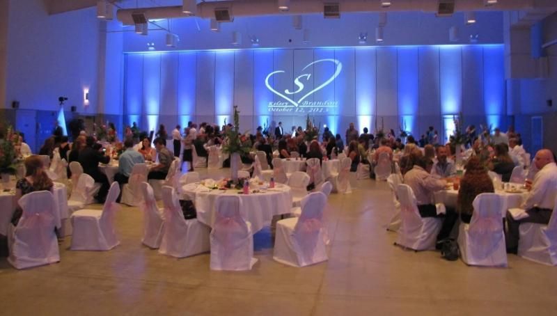 Elegant banquet hall with round tables, guests seated, and a blue-lit stage with a projected logo.