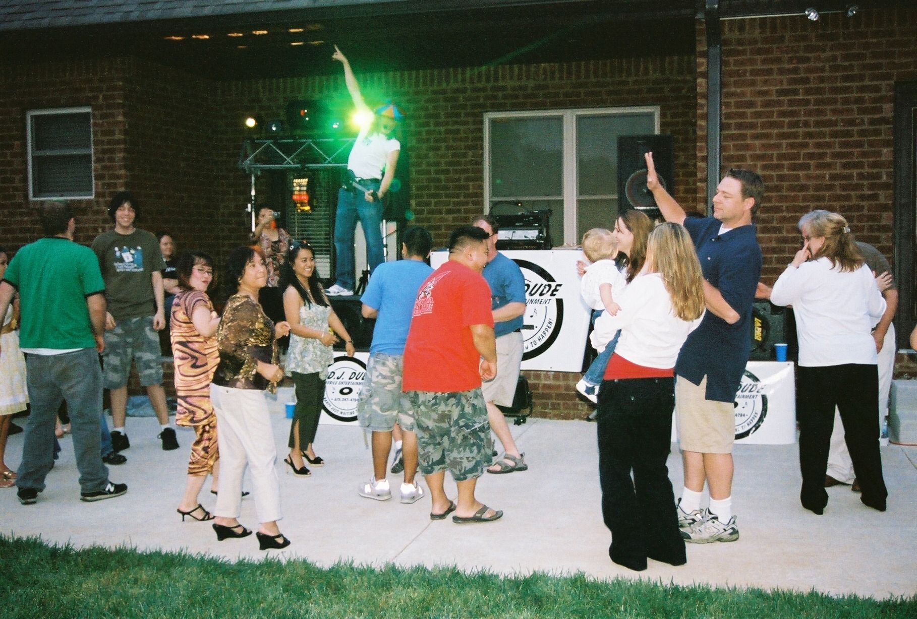 People dancing outdoors in front of a brick building at night, with colorful lights and a banner in the background