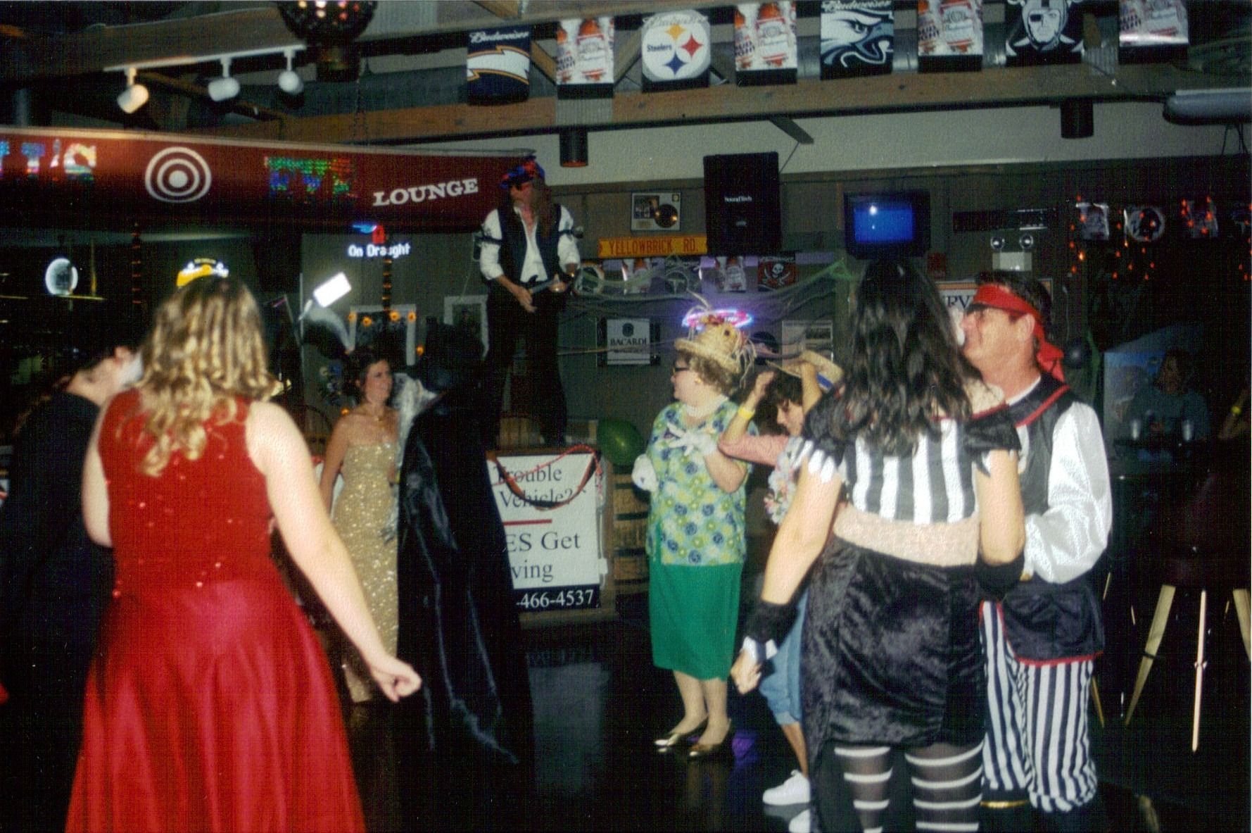 People in costumes dancing in a crowded bar, with dim lights and Halloween decor.