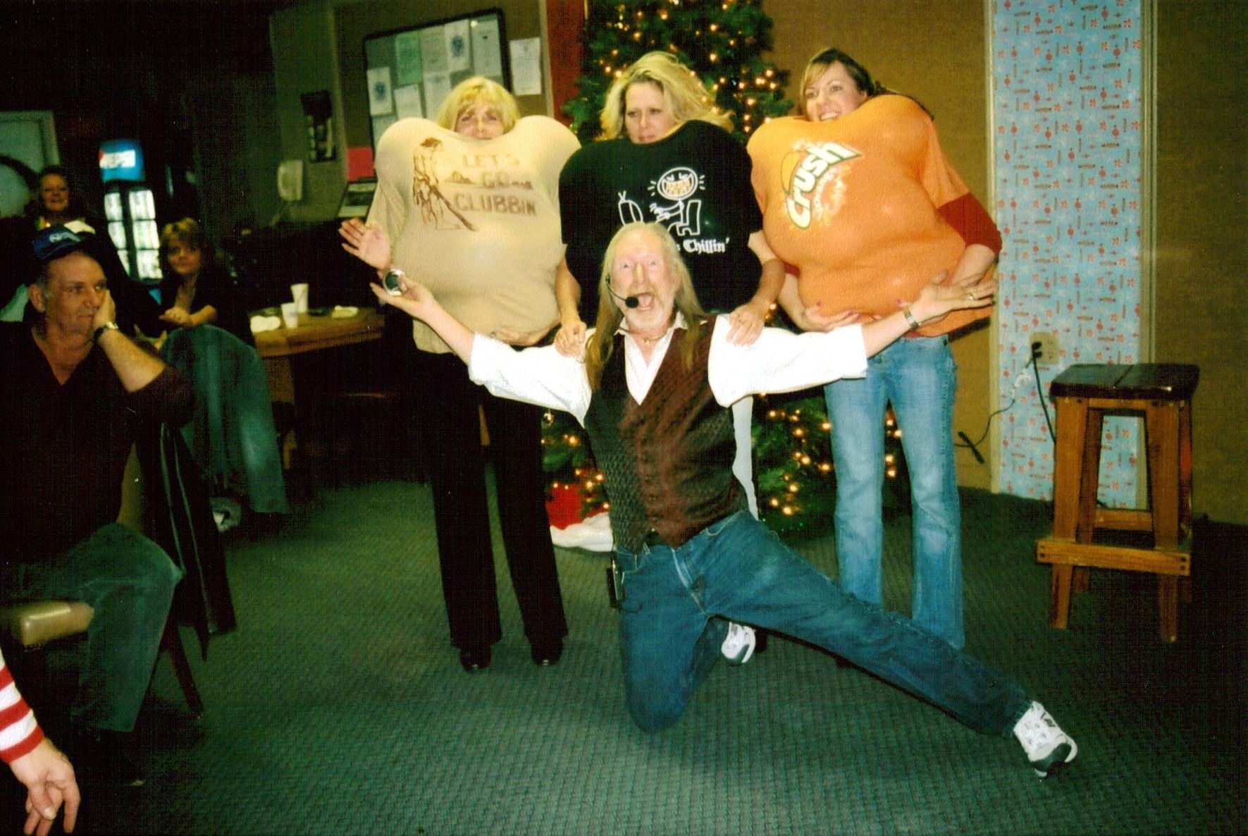 Person kneels with arms outstretched in a room while three people stand behind holding papers.