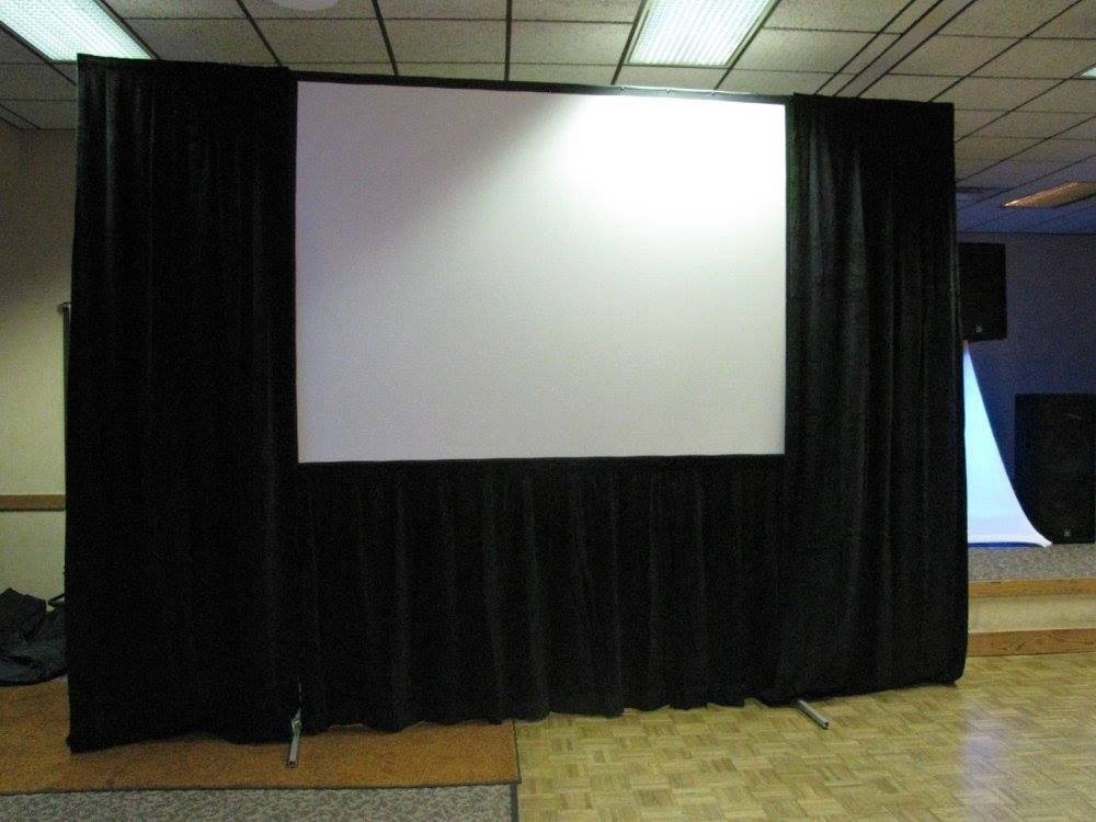 Empty stage with a large white projection screen and black curtains in a conference room