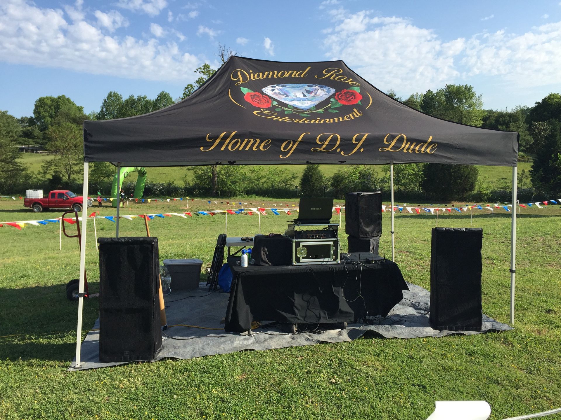 Black event tent with speakers and DJ table on a grassy field, “Home of M.Y. Tribe” banner on front.