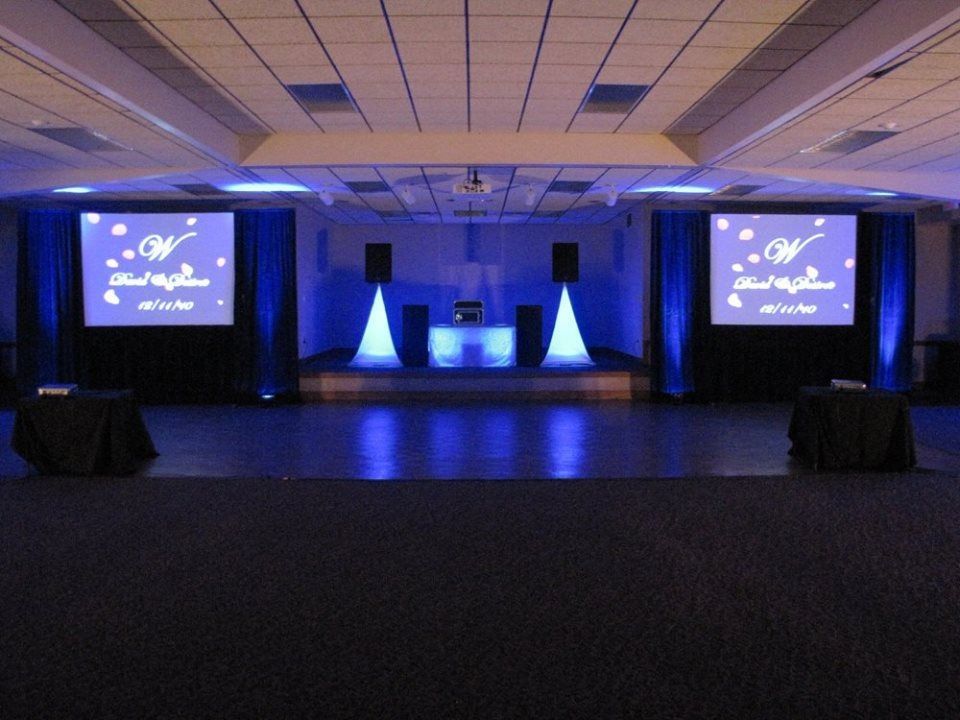 Blue-lit event hall with two projection screens and a central stage