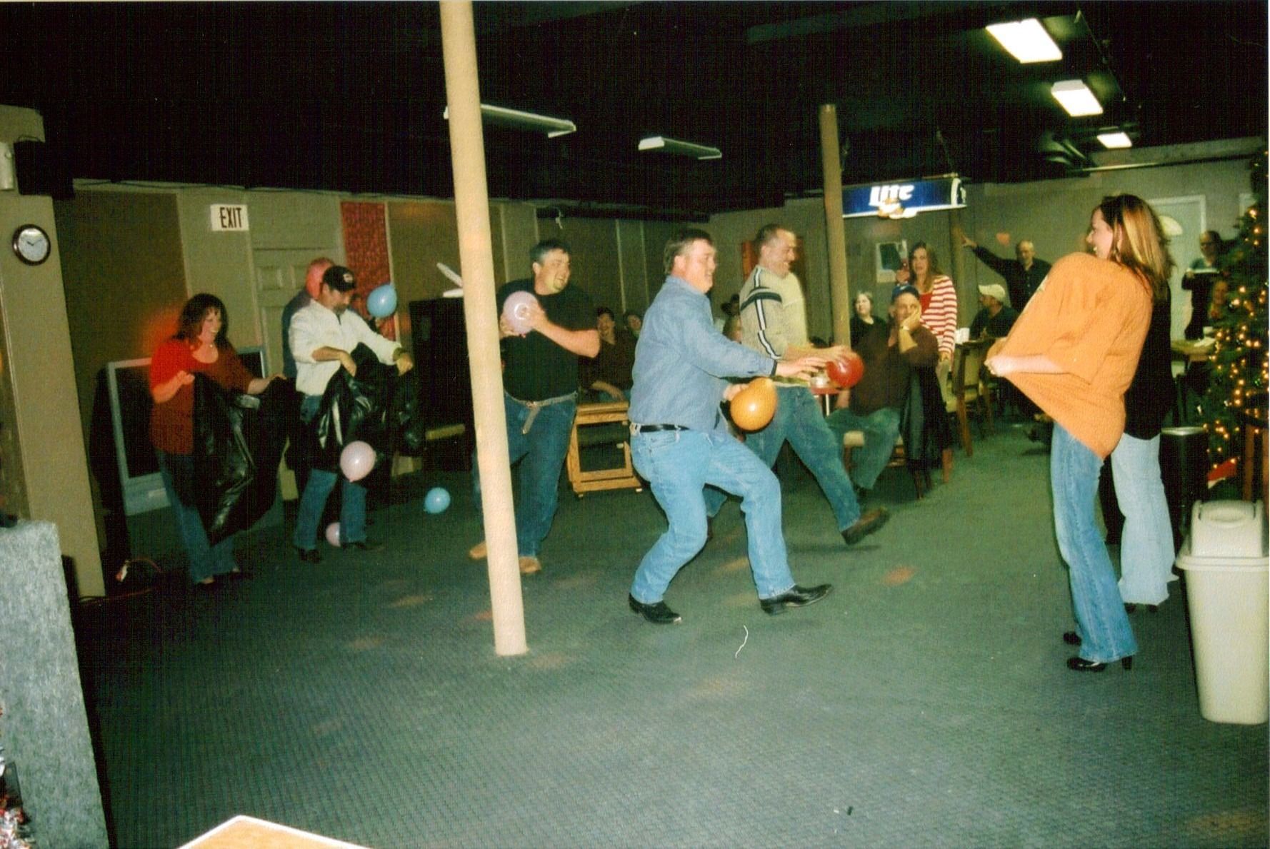 People playing dodgeball in a dim indoor recreation hall, with one person throwing an orange ball.