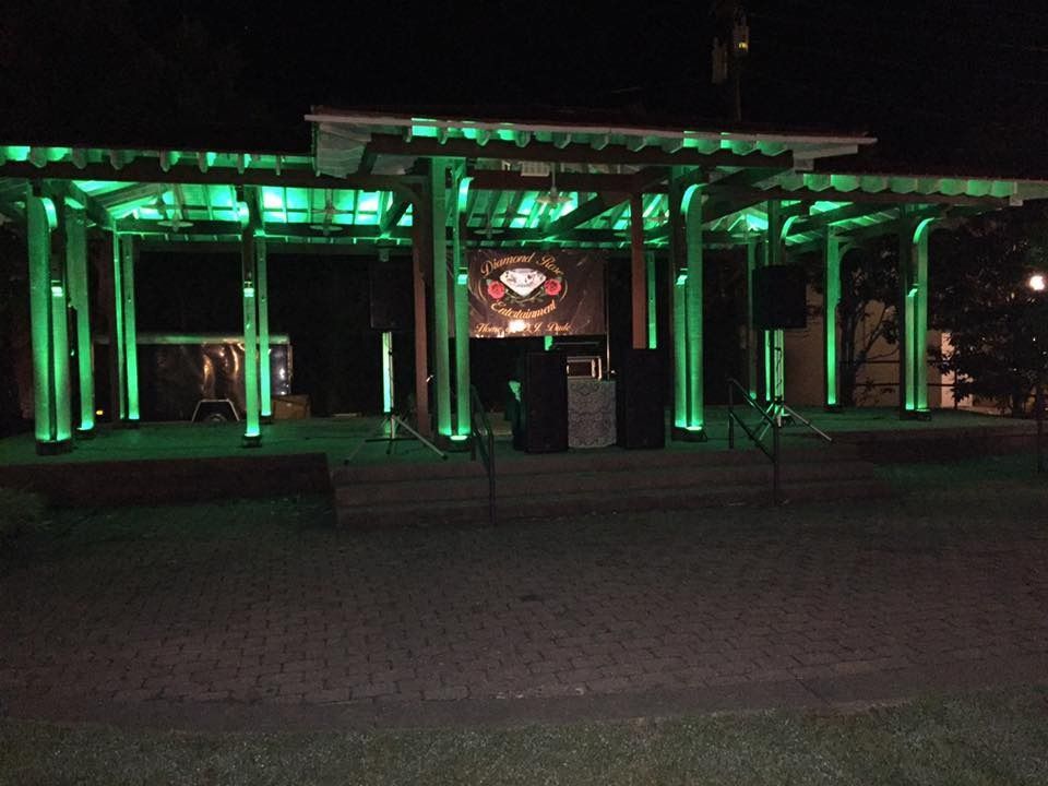 Nighttime view of a green-lit pavilion with a stage or screen in front of a dark plaza