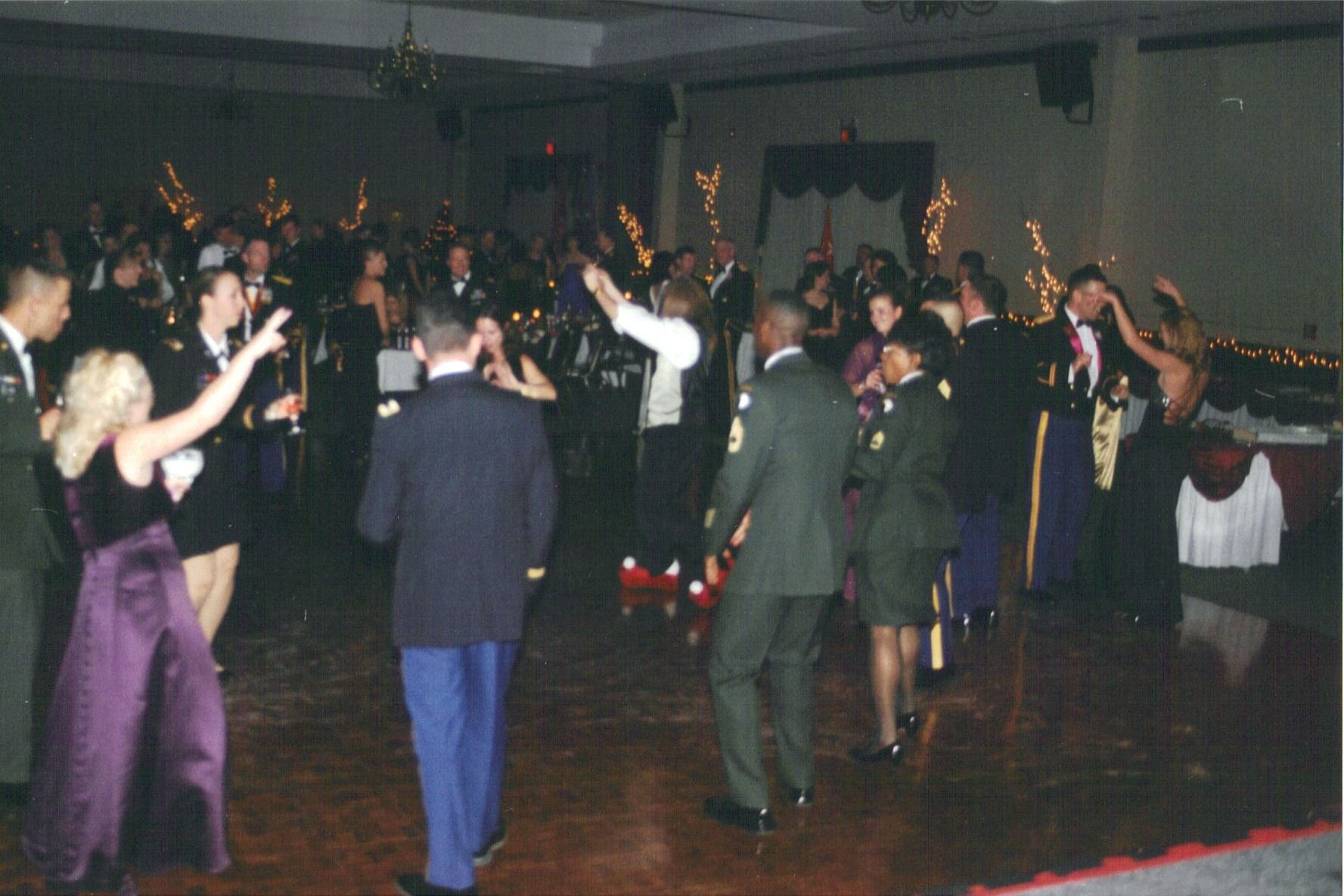 People dancing in a dimly lit hall at a formal event, with tables and decorations in the background