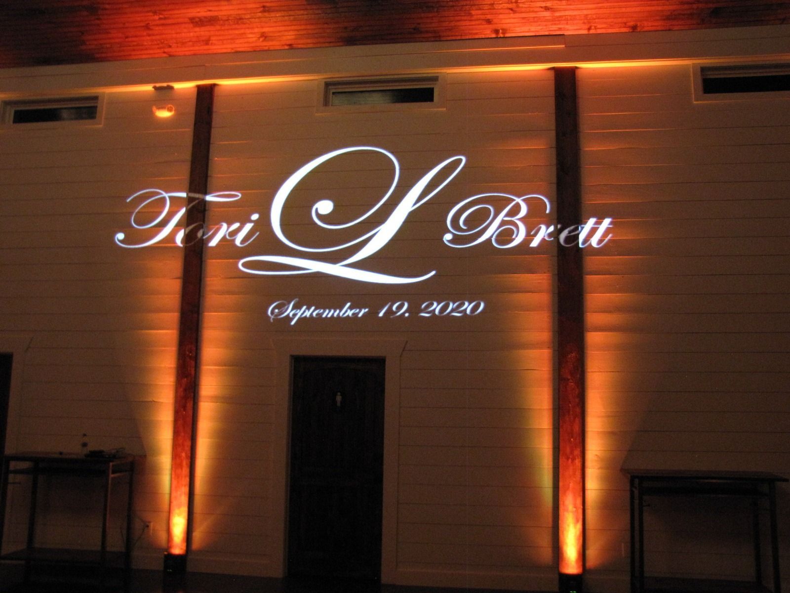 Illuminated sign on a building facade reading “Fiori L Brat” with warm orange uplighting.