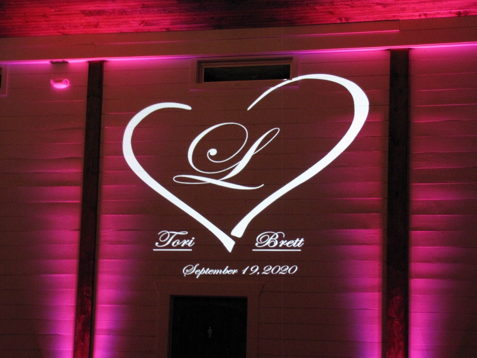 Pink-lit wall with a glowing white heart and monogram, plus names and wedding date text.