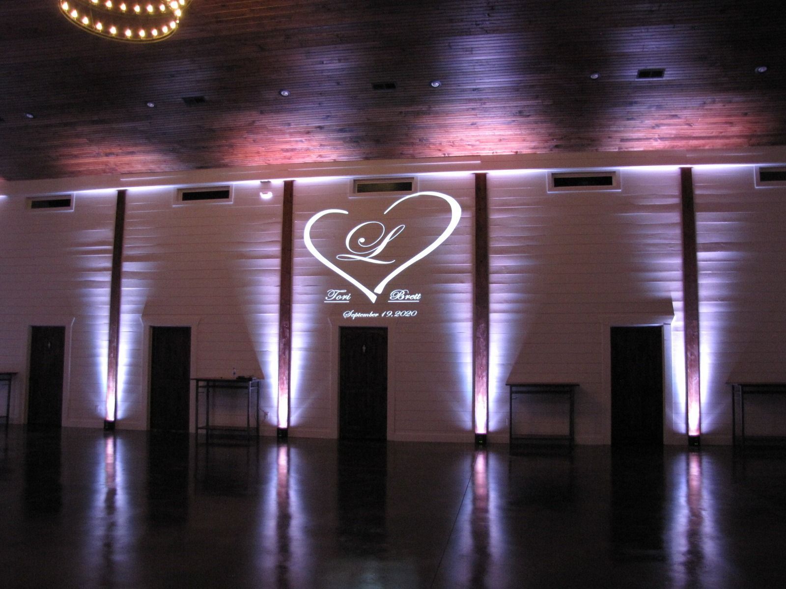 Dimly lit event hall wall with a white heart logo projected above dark doorways and purple uplights