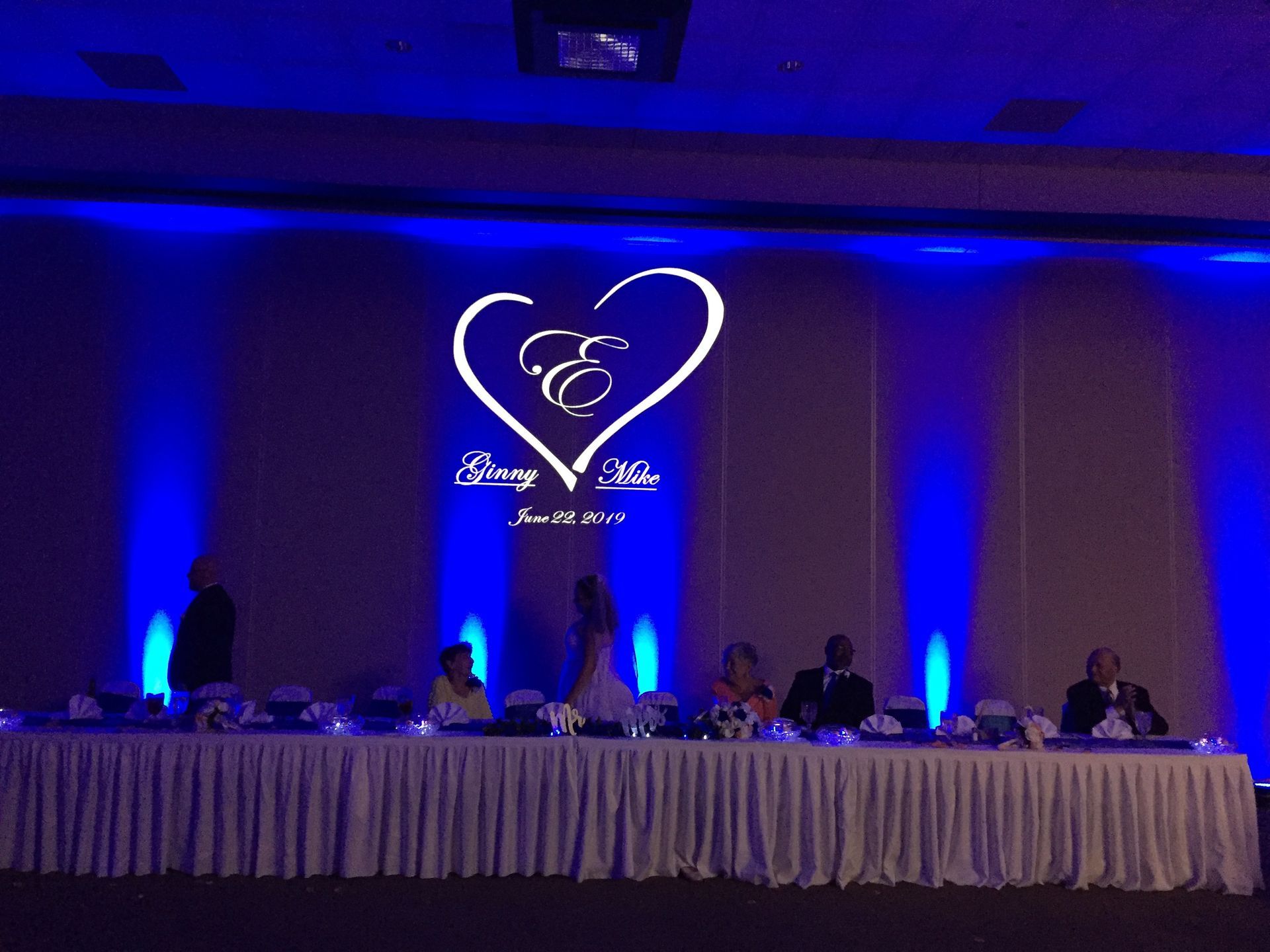 Blue-lit banquet stage with a long table of seated panelists and a heart-shaped logo backdrop