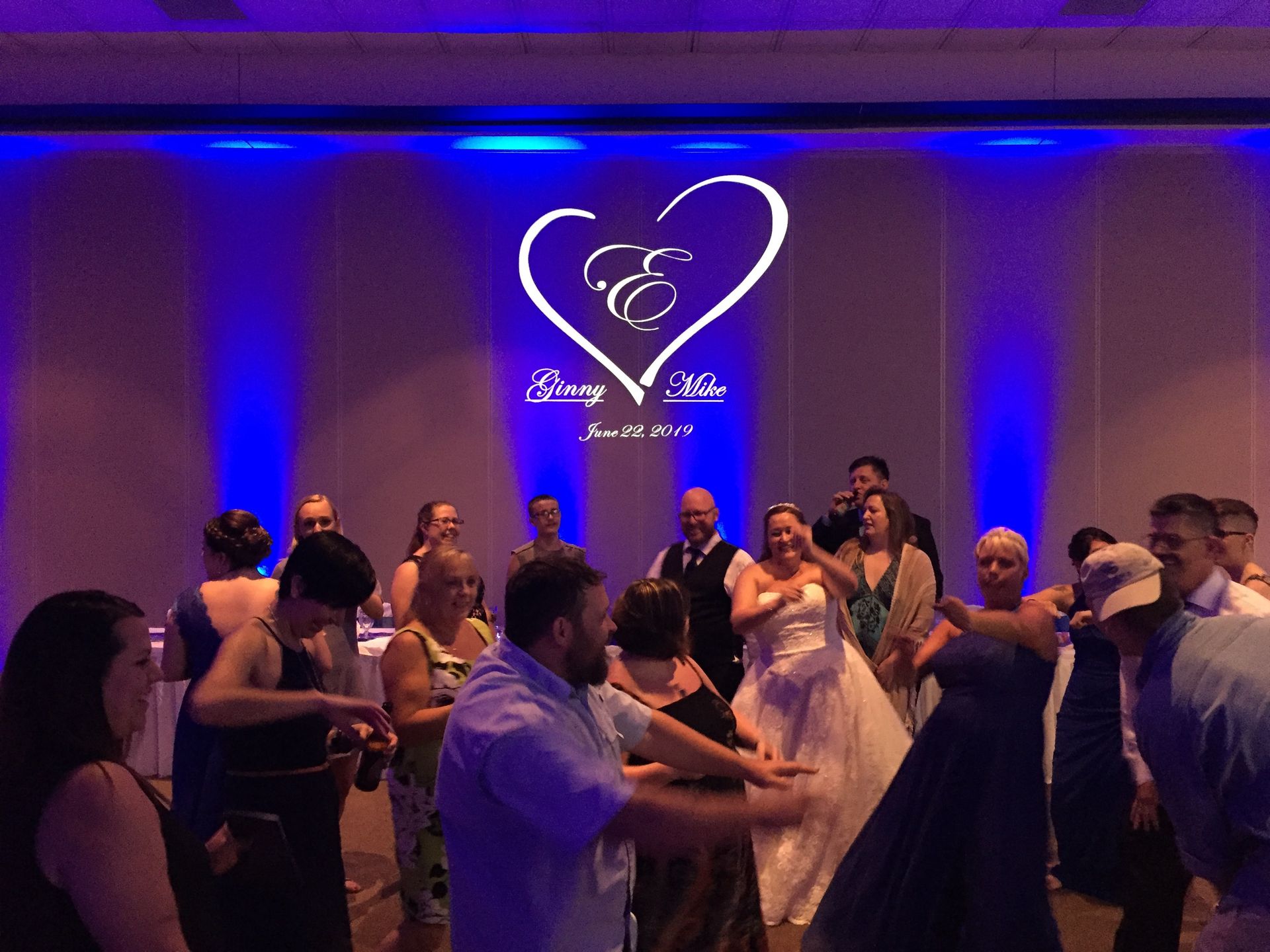 Wedding guests dancing in a blue-lit reception hall with a heart-shaped logo on the wall