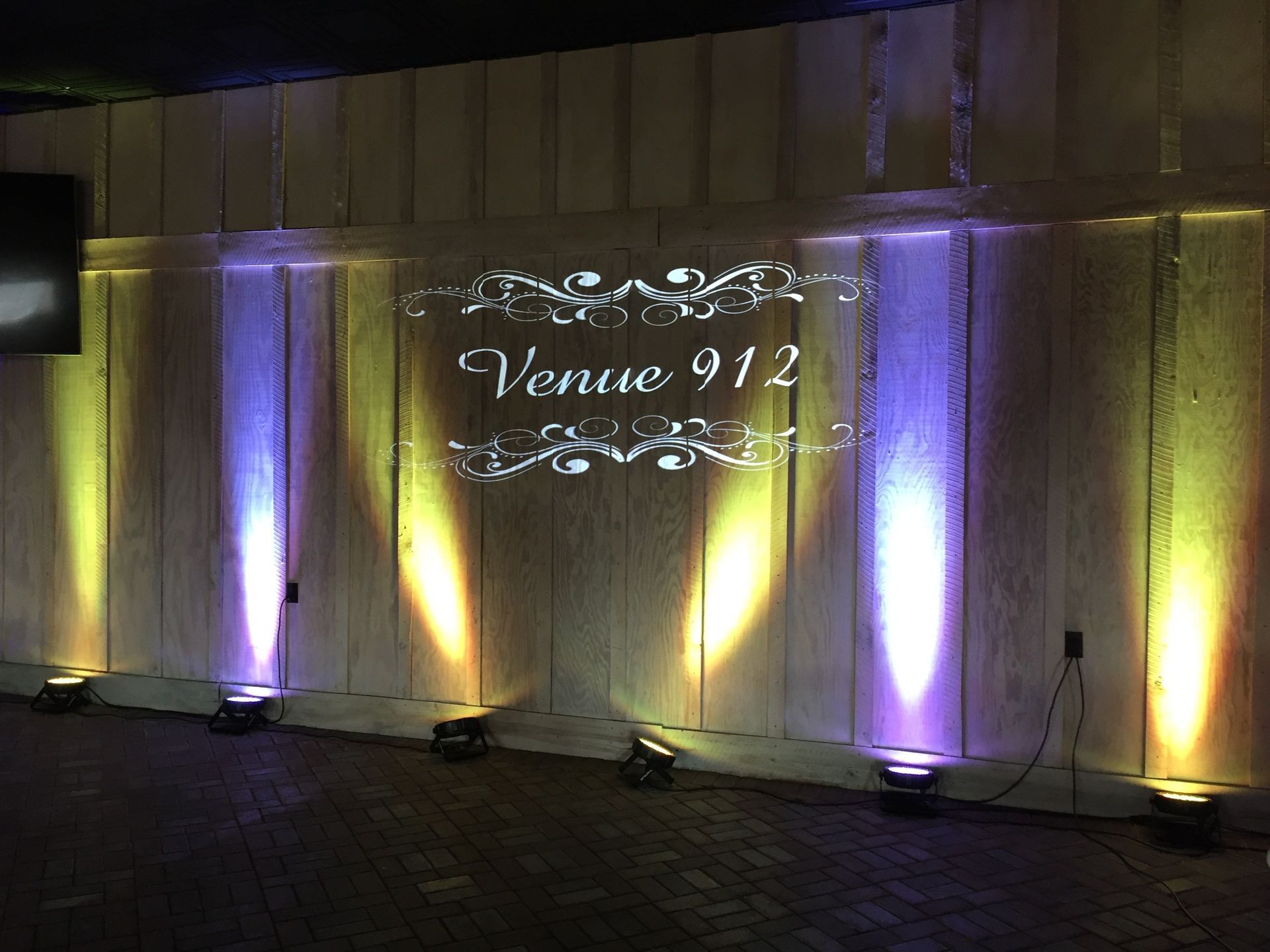 Illuminated venue wall with purple and yellow uplights and a sign reading “Venue 912”