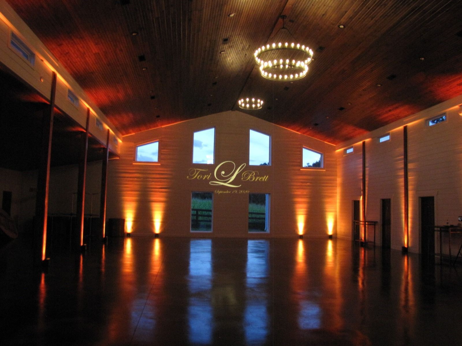 Empty event hall with warm orange uplighting, glossy floor, and a chandelier ceiling.