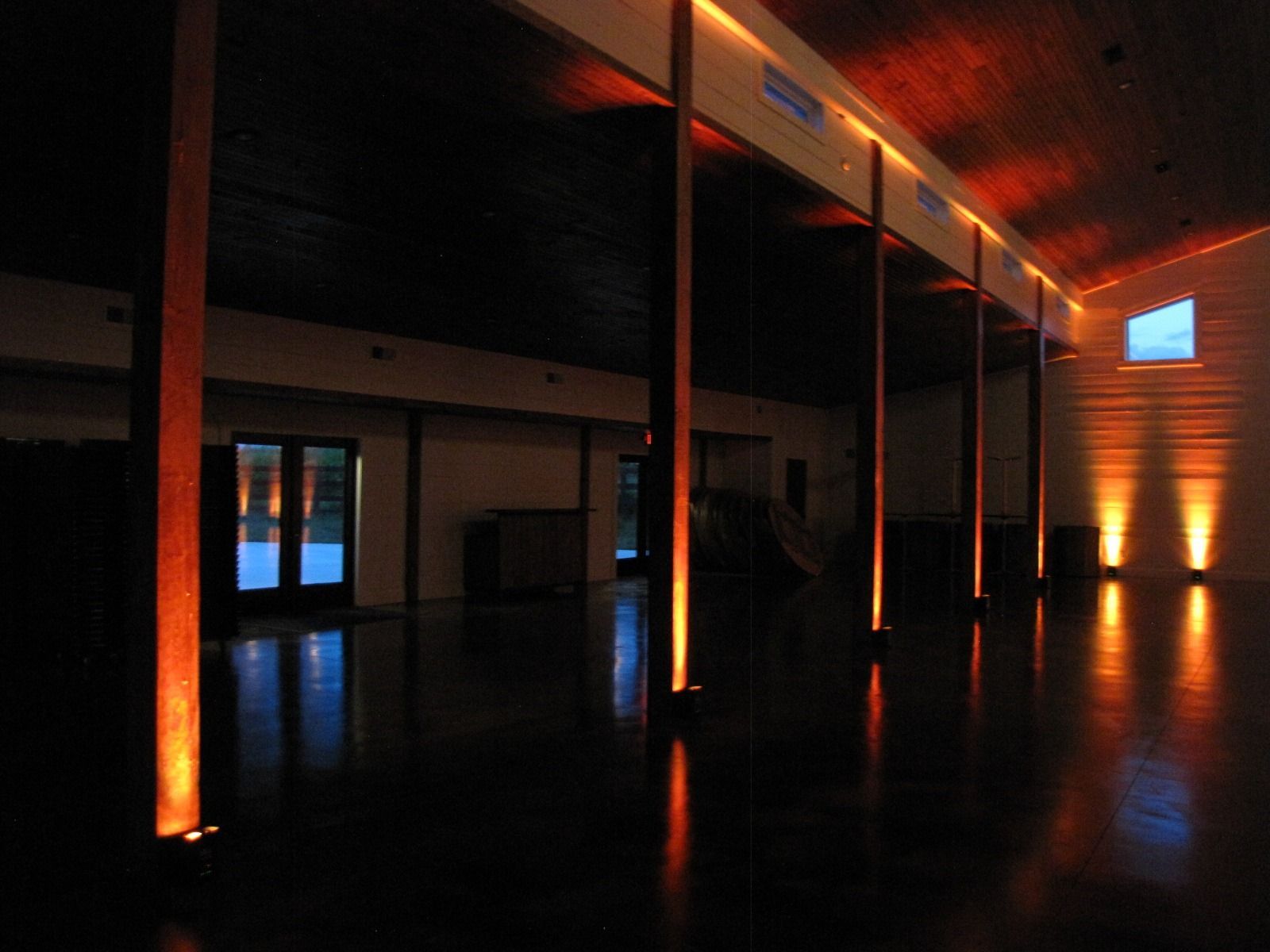Dim modern lobby with orange uplighting, reflective black floor, and glass doors at left.