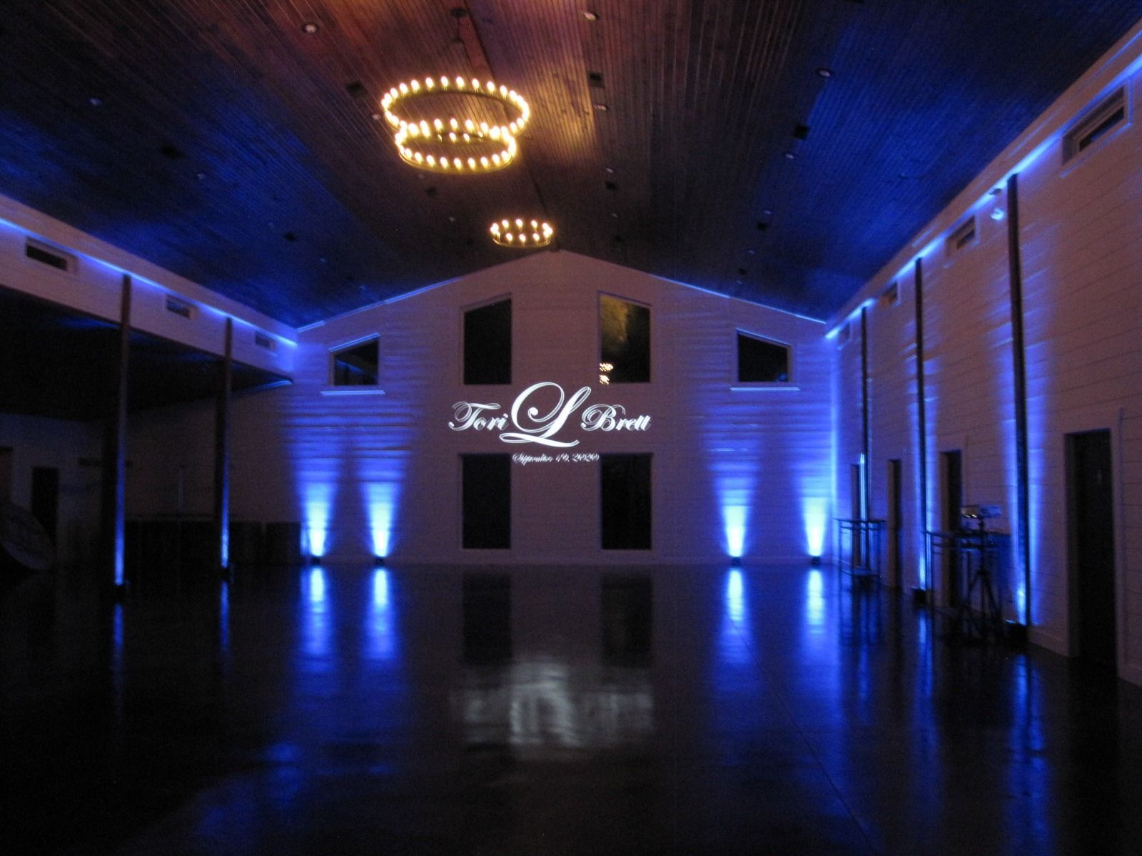 Dimly lit event hall with blue uplighting, a polished floor, and a lit chandelier-style ceiling fixture.