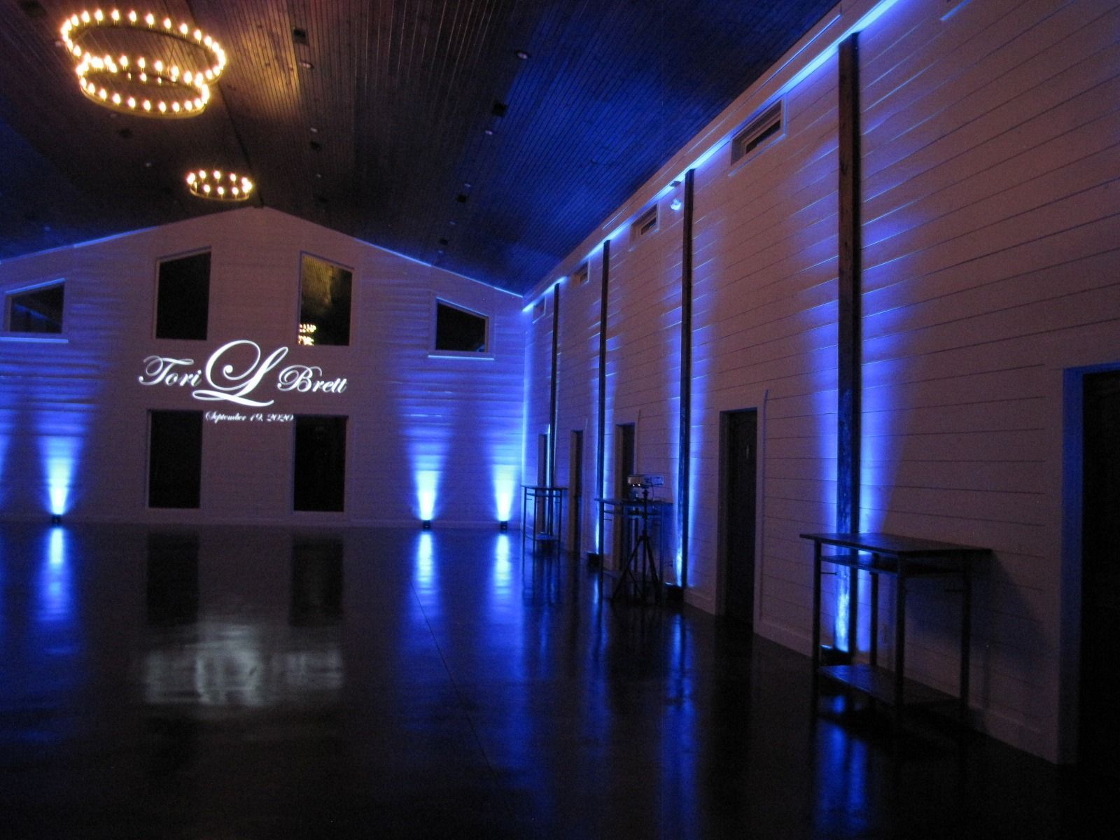 Dim blue-lit event hall with glossy black floor and a lit sign on the back wall