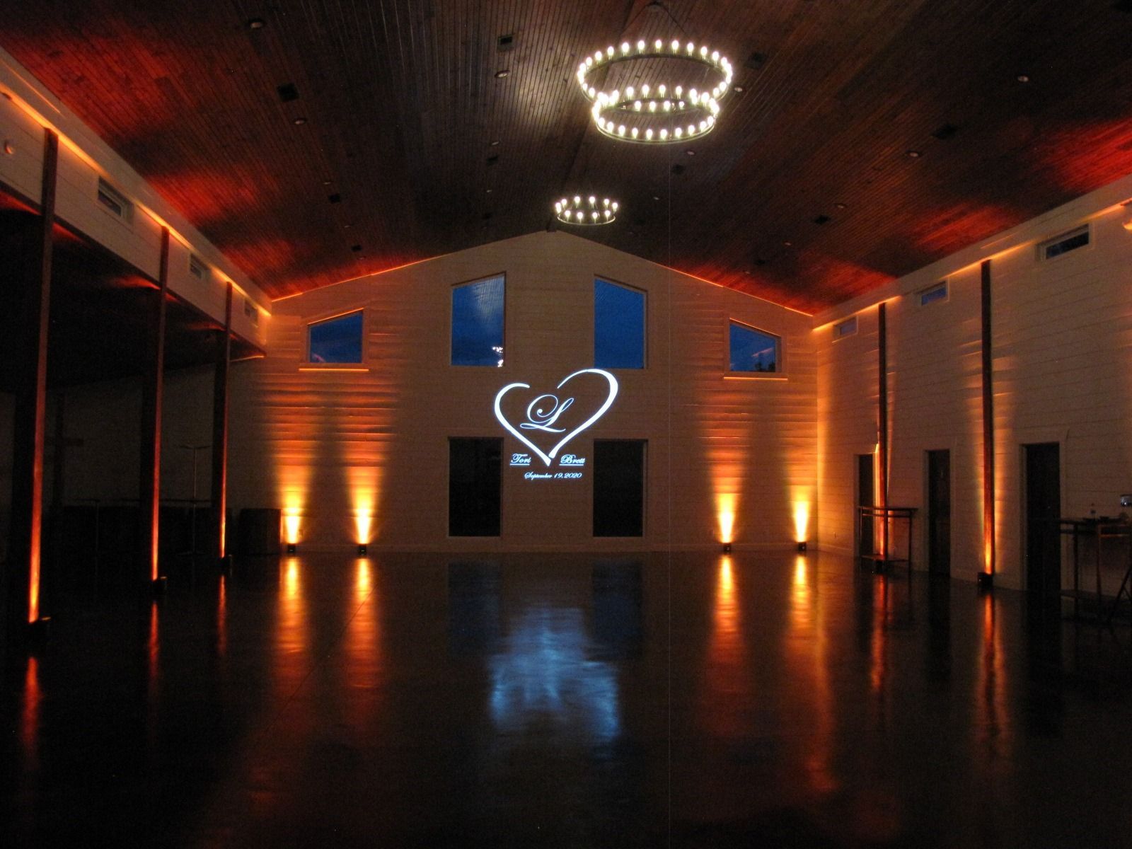 Empty banquet hall with chandeliers, blue-lit windows, and heart-shaped light decoration on the back wall.