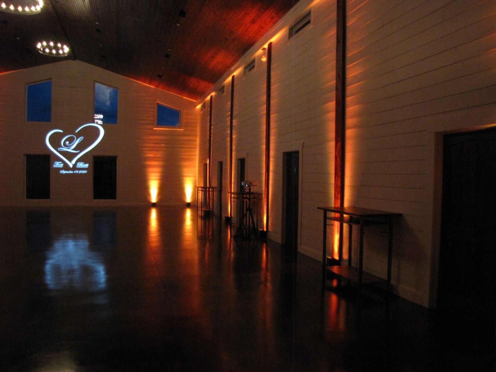 Dimly lit modern hall with warm orange lights, glossy floor, and a glowing heart logo projection on the wall