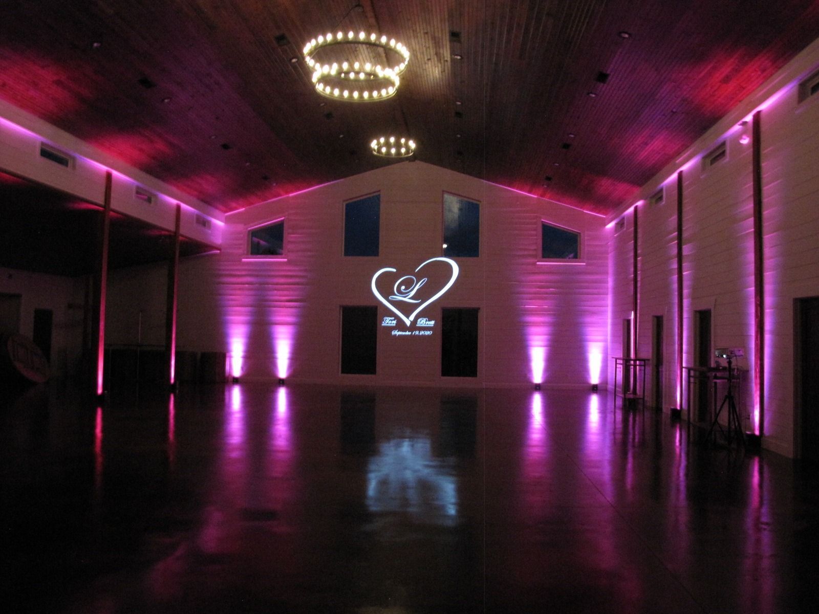 Elegant empty hall with purple uplighting, chandeliers, and a heart logo projected on the far wall