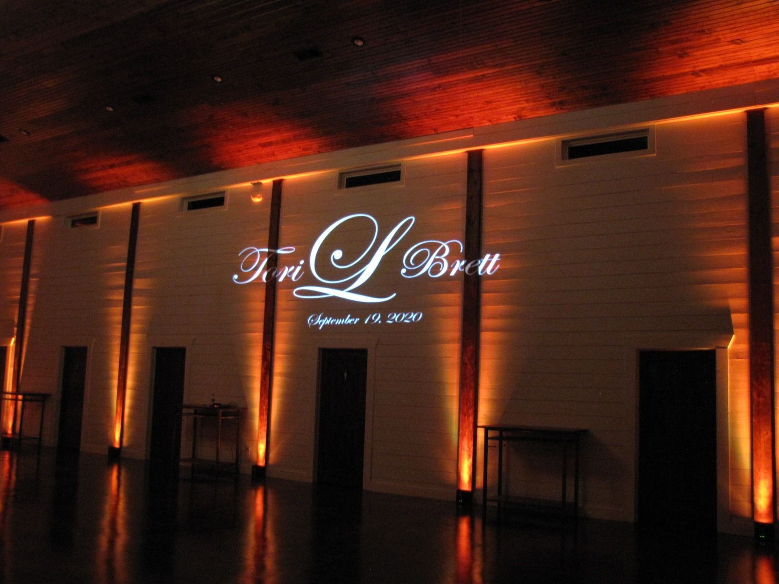 Dimly lit banquet hall with a glowing sign on a wood-paneled wall and warm orange ceiling lights.