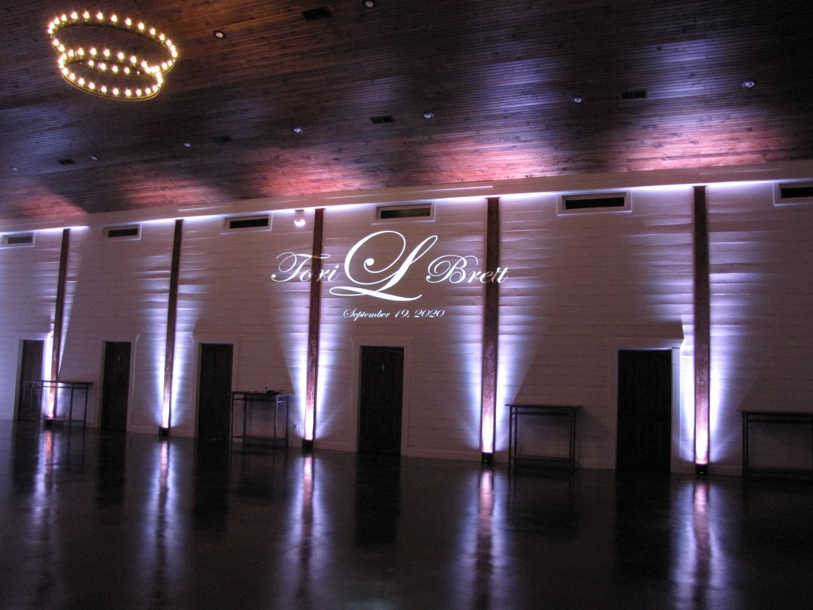 Lit event hall with purple uplighting, a glossy floor, and a glowing script sign on the back wall