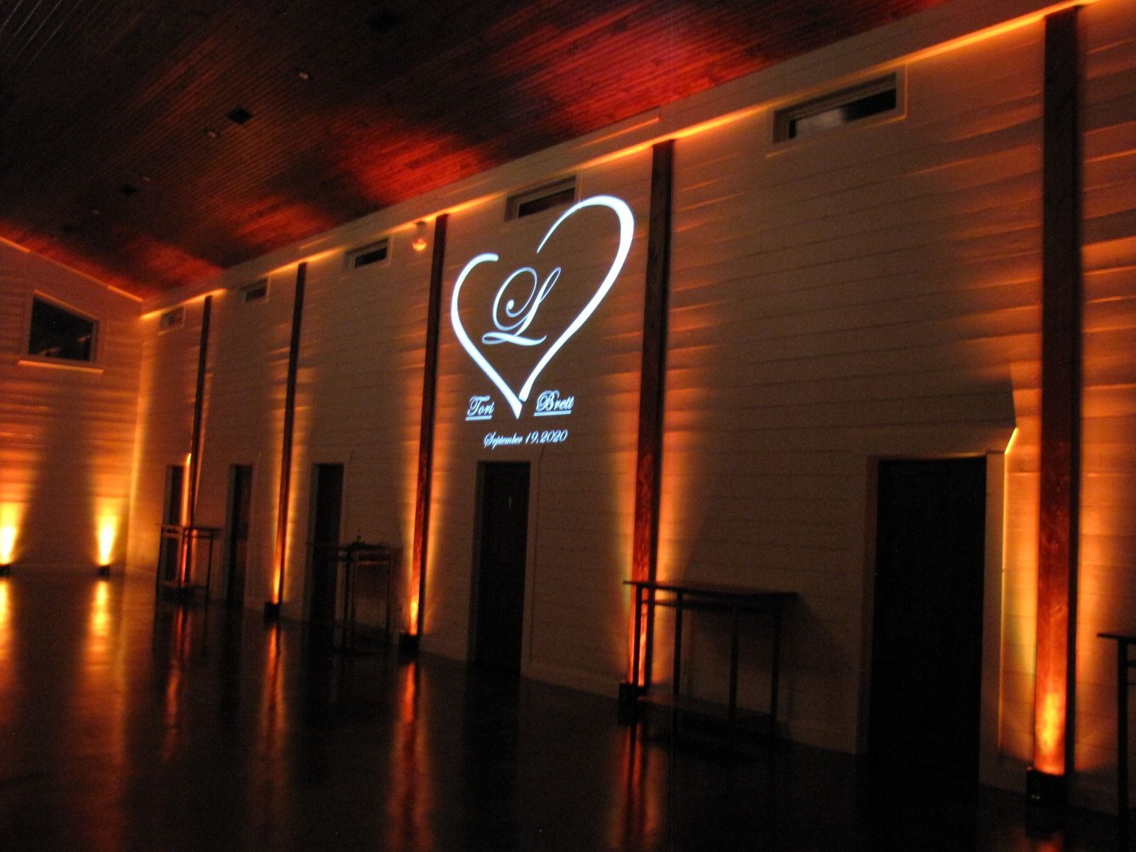 Dimly lit event hall with orange uplighting and a glowing heart logo on the wall