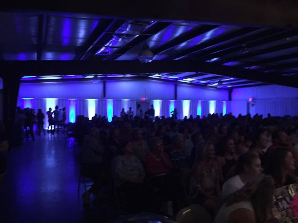 Crowded conference hall with blue-purple lighting and people seated in the audience