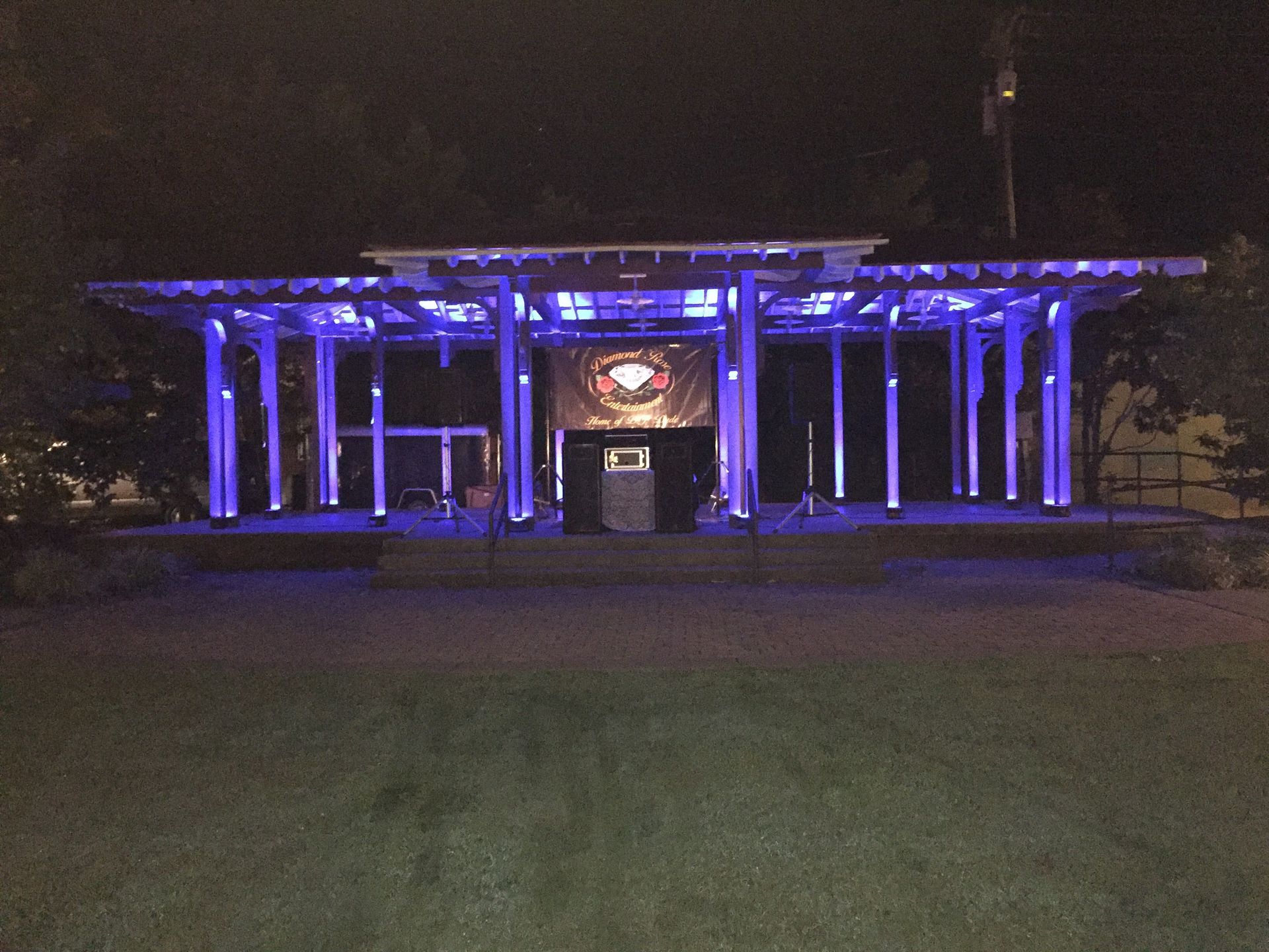 Purple-lit pavilion at night with a glowing sign and dark lawn in front
