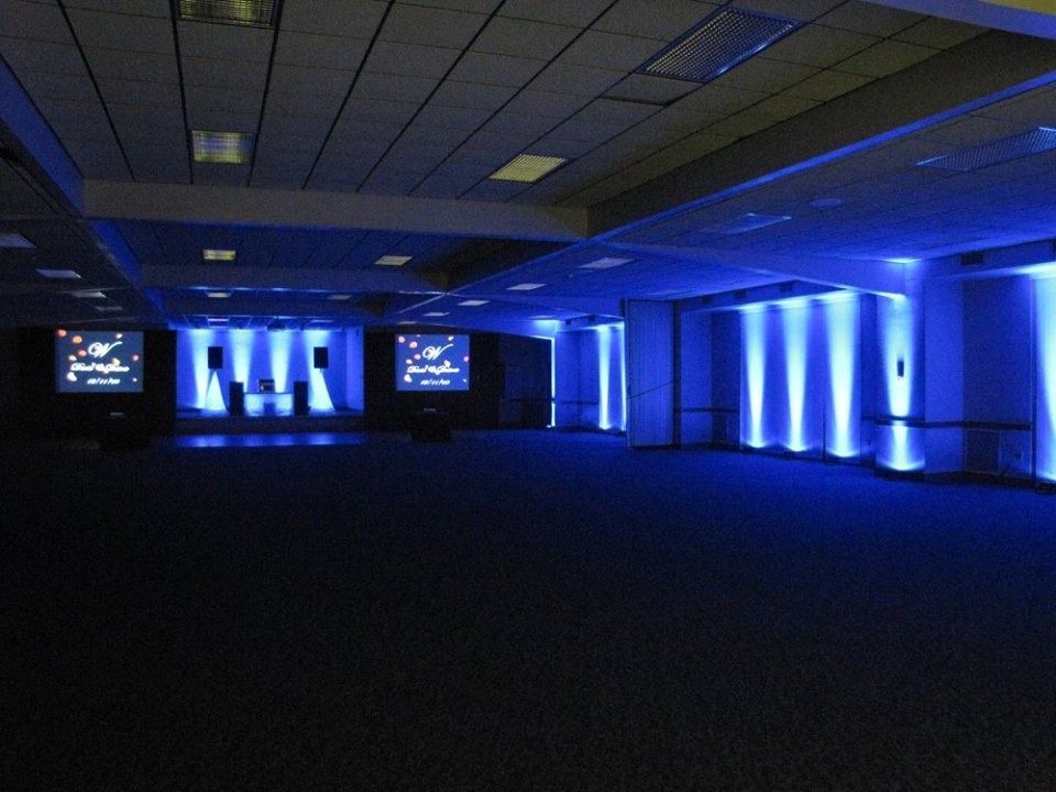 Blue-lit conference hall with stage, screens, and rows of empty floor seating