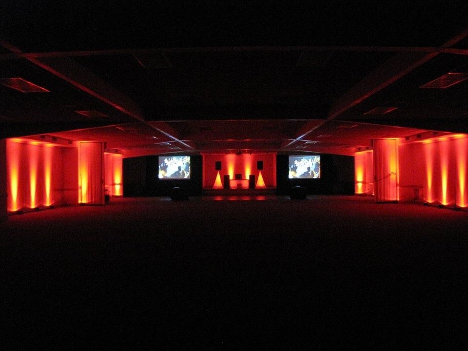 Dim event hall with red uplighting and two projection screens on the far wall
