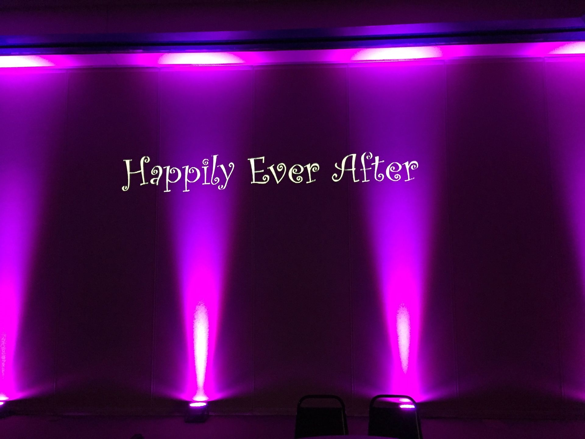 “Happily Ever After” text projected in white on a purple-lit wall with stage spotlights.