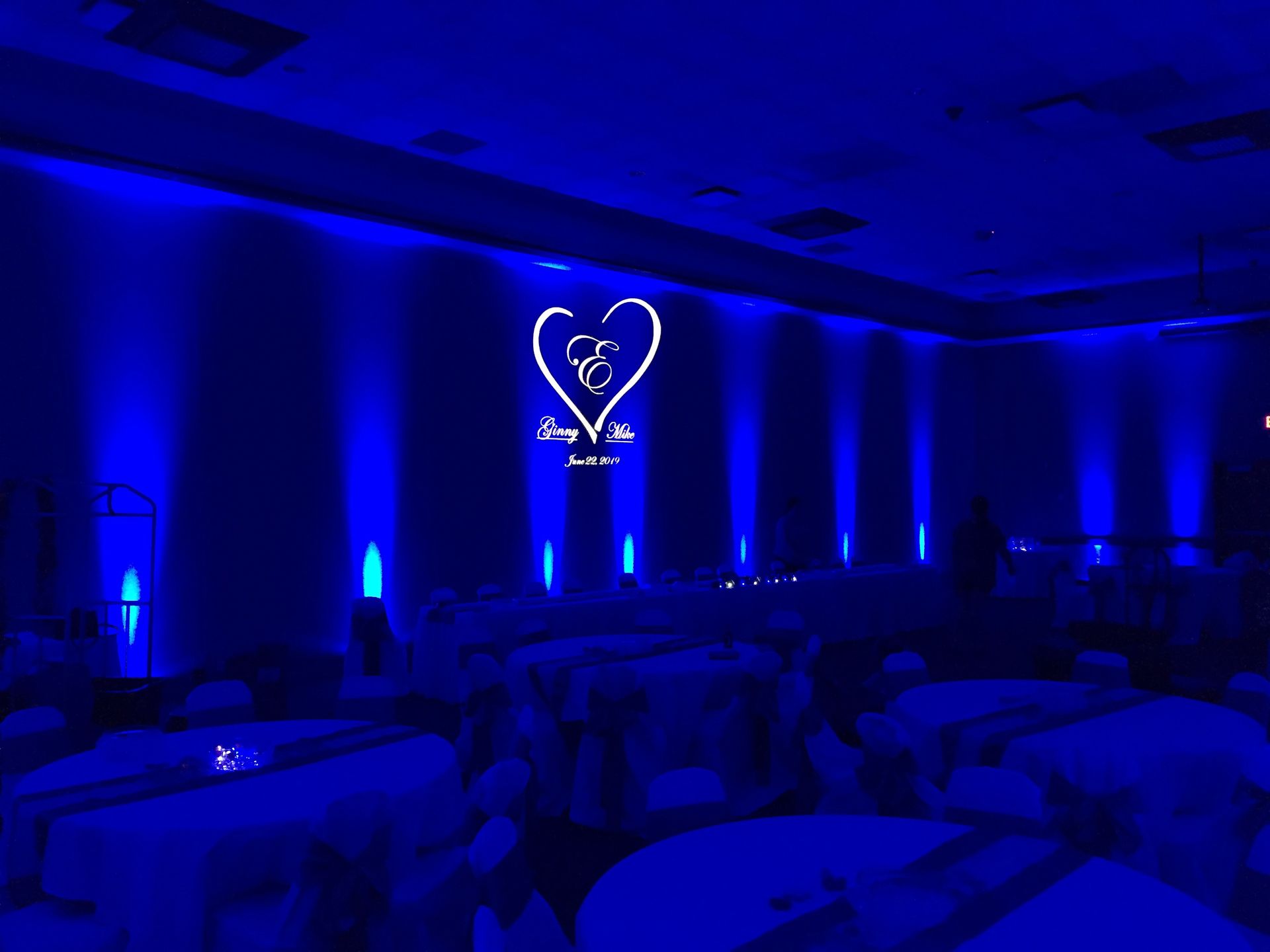 Blue-lit banquet hall with round tables and a glowing heart-shaped logo on the wall
