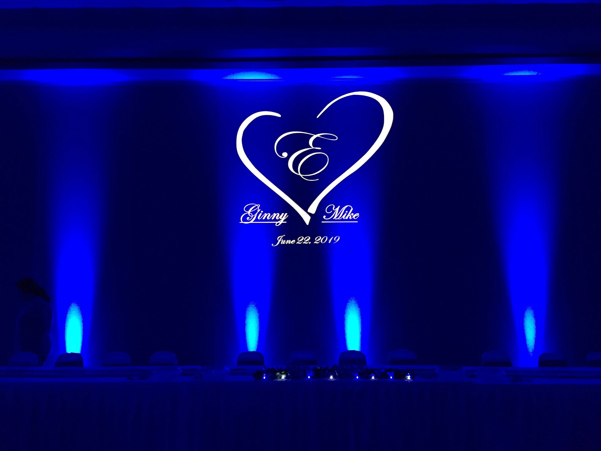 Blue-lit stage with a heart-shaped logo and white script centered on a dark backdrop