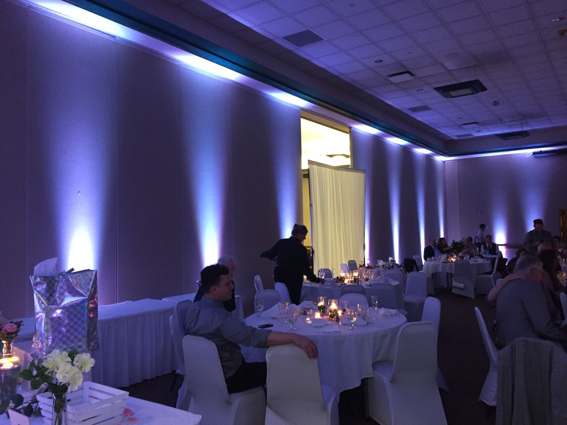 Dimly lit banquet hall with guests seated at round tables and purple uplighting along the walls